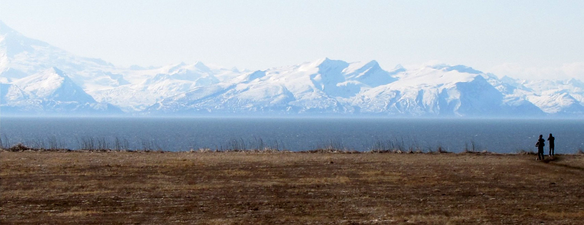 Mountains shrouded in fog are seen across Cook Inlet as two people walk the shoreline of Kenai.